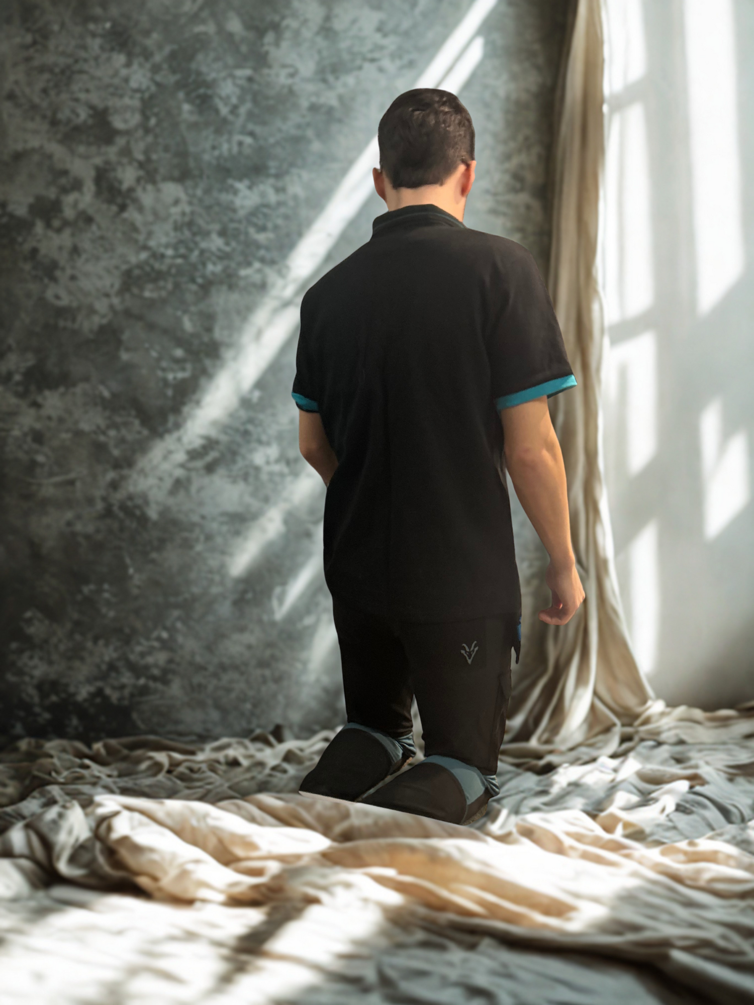 Man in black Goat Workwear outfit standing in a room with sunlight filtering through curtains.