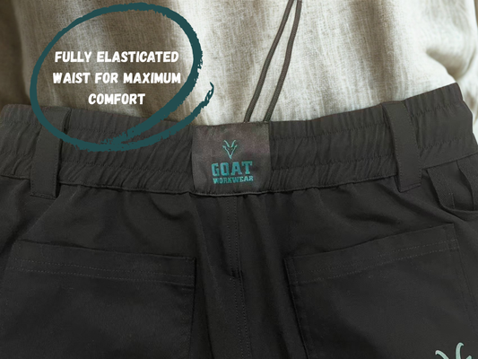 Black construction workwear trousers  with a fully elasticated waistband and a visible brand label on a person wearing a light-colored shirt.